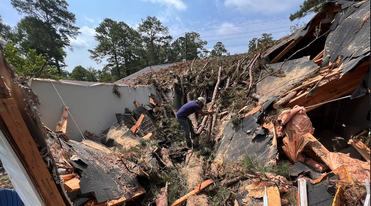 Catastrophic storm damage to a home with fallen pine trees and exposed roof framing